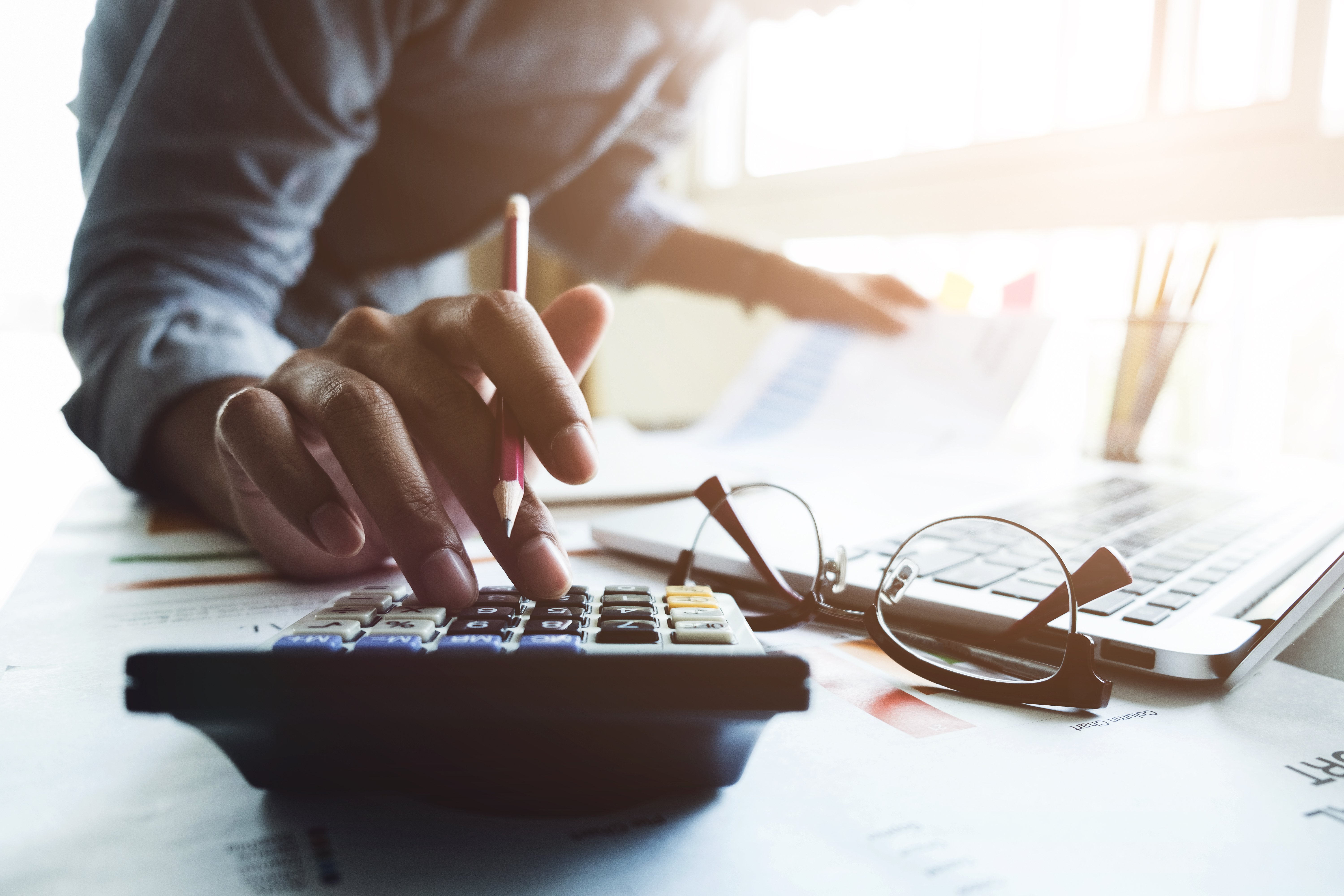 Person calculating finances with laptop and paperwork