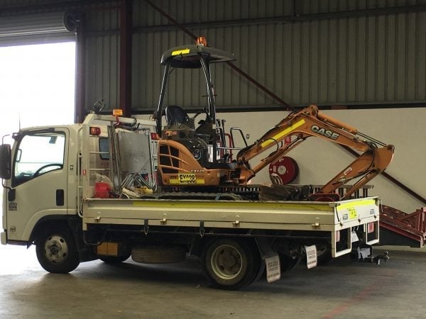 Flatbed truck carrying mini excavator in shed