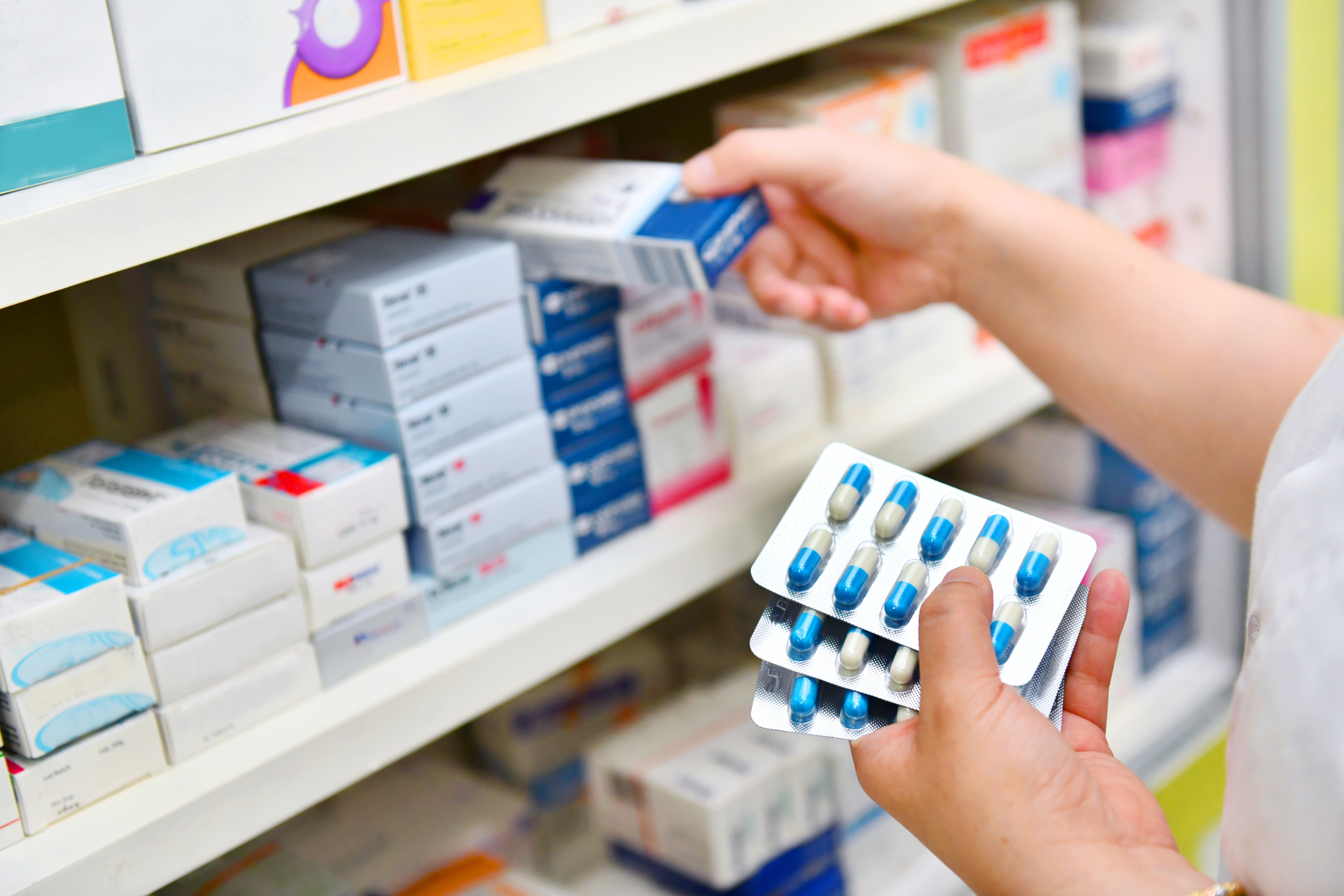 Person selecting capsule packs from pharmacy shelf