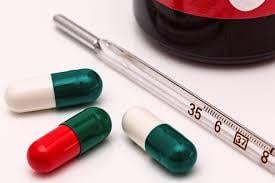 Thermometer and capsules beside medicine bottle