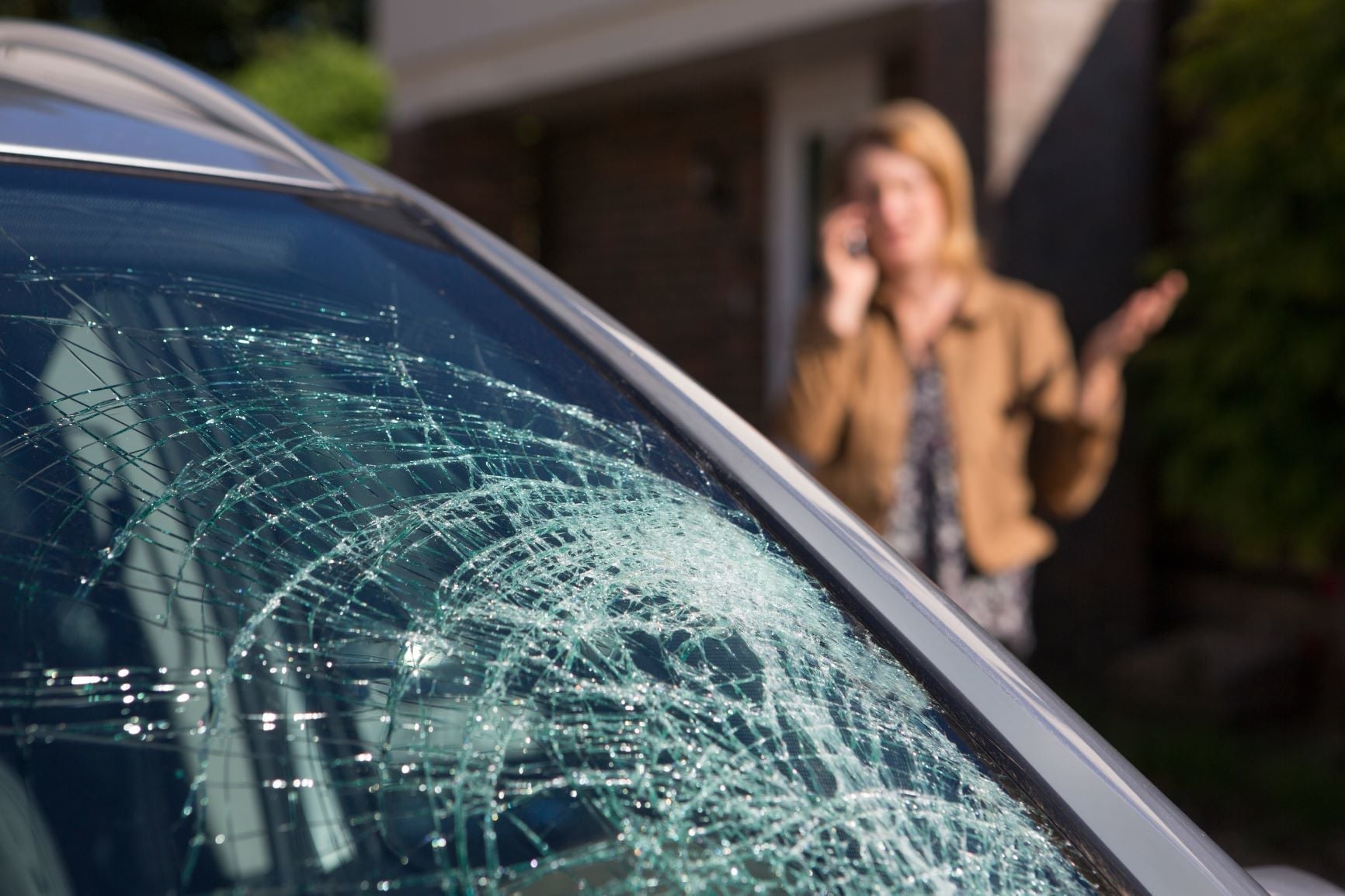 Cracked car windscreen with woman on phone nearby