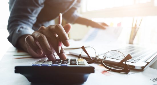 Person calculating finances with laptop and paperwork