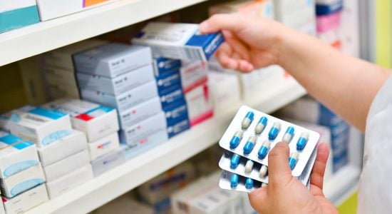 Person selecting prescription capsules from pharmacy shelf