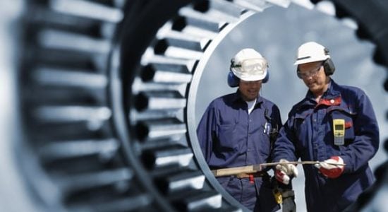 Two engineers inspecting large industrial gear machinery